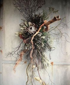 a dried wreath hanging on the side of a building with branches and flowers attached to it