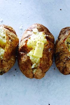 three baked potatoes with cheese and seasoning on them sitting next to eachother