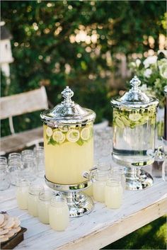 a table topped with lots of glasses filled with lemonade next to jars full of lemons