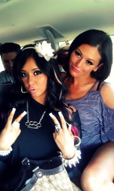 two women sitting in the back seat of a car with one pointing at the camera