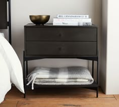 a nightstand with two books on it next to a white bed and a black night stand