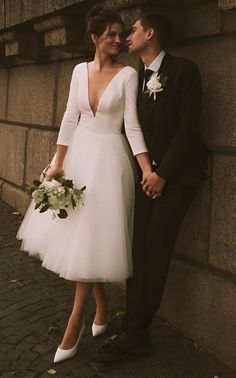 a man and woman standing next to each other near a stone wall with flowers in their hands