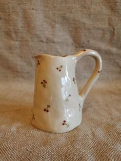 a small white pitcher sitting on top of a brown tablecloth covered bed sheet with red and green flowers