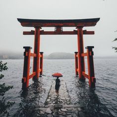 a person with an umbrella standing in the water near a large torin structure that looks like it has been built into the water