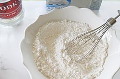 a white bowl filled with flour next to a whisk and bottle of soda