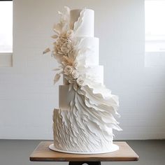 a three tiered white wedding cake with flowers on the top and bottom, sitting on a wooden table