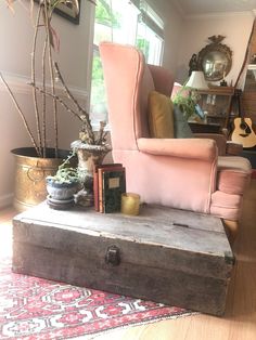 a pink chair sitting on top of a wooden trunk in a living room next to a window