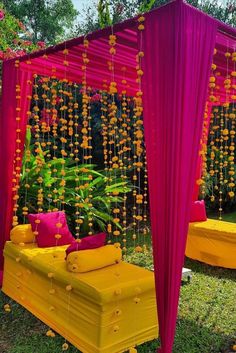 a yellow and pink bed sitting under a canopy in the grass next to flowers on the ground