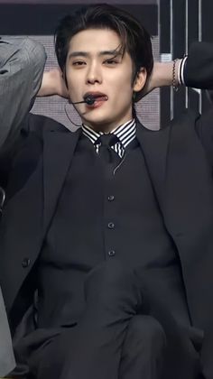 a man in a suit and tie sitting down with his hands on his head as if he is listening to music