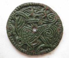 an ancient coin with intricate designs on the front and side, sitting on a white surface