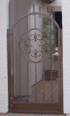 an iron gate is open on the side of a house with a potted plant behind it