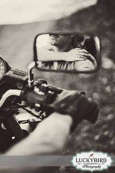 a man taking a photo in the side mirror of a motorcycle with his hand on the handlebars