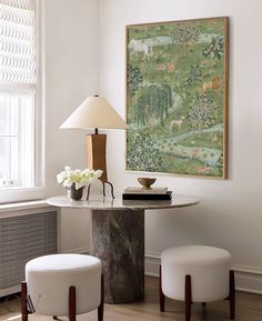 a table with two stools and a painting on the wall in a living room