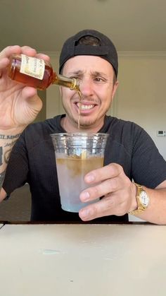 a man sitting at a table with a drink in front of his face and holding a bottle