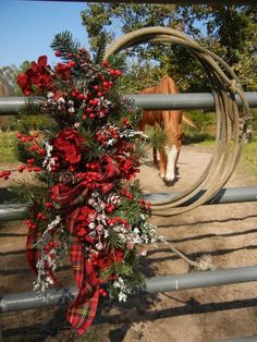 a wreath with red flowers and greenery tied to it on a fence near a horse