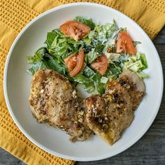 a white plate topped with meat and salad next to a yellow napkin on top of a wooden table