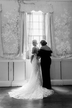 two women standing next to each other in front of a window with curtains on it