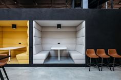 three chairs and a table in a room with black walls, white tables and yellow booths