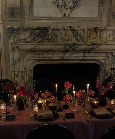 a table set with candles and flowers in front of a fireplace