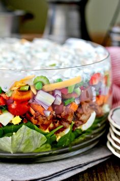 a salad in a glass bowl sitting on top of a table next to plates and utensils