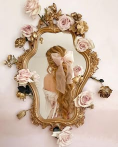 a woman with long blonde hair standing in front of a mirror covered in pink flowers