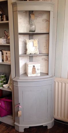 the corner cabinet is painted gray and has an open shelf above it, along with other items