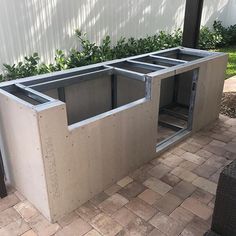 an outdoor kitchen made out of cinder blocks and steel grates on the ground next to a brick patio