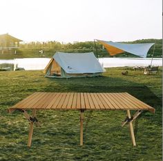 two tents are set up in the grass near a body of water and a picnic table