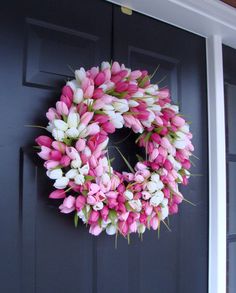 a pink and white tulip wreath hangs on the front door of a black house