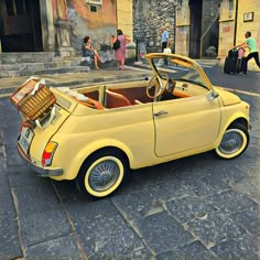 an old yellow car parked on the street with luggage in it's back seat