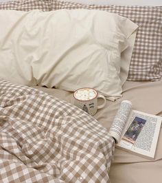 an open book, coffee cup and plate on a bed with gingham sheets