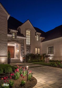 a house that is lit up at night with flowers in the front yard and landscaping around it