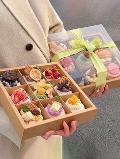 a person holding a box filled with cupcakes and pastries in it's hands