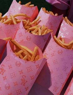 pink paper bags filled with french fries sitting on top of each other in front of a purple bag