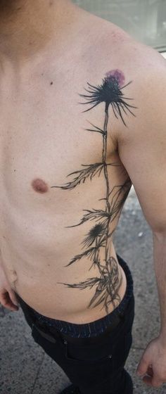 a man with a flower tattoo on his chest is standing in front of a car