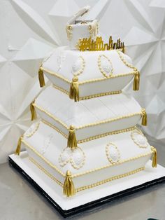 a three tiered cake with gold trimmings and tassels on top