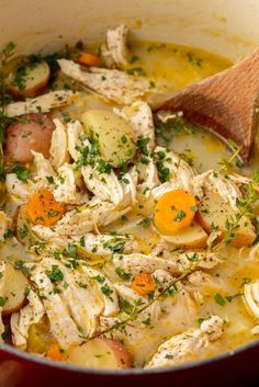 a pot filled with chicken, potatoes and carrots next to a wooden ladle