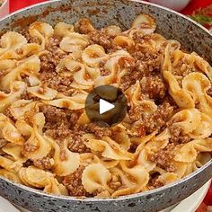 a large pot filled with pasta and meat on top of a table next to vegetables