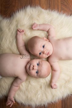 two babies laying on top of a fluffy white rug in front of a wooden floor