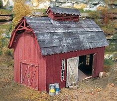 a red barn with a black roof and two doors on the side of it, in front of some rocks