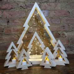 three white wooden christmas trees with candles in the middle and one lit up at the bottom