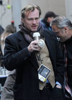 a man holding a camera and looking at his cell phone while walking down the street