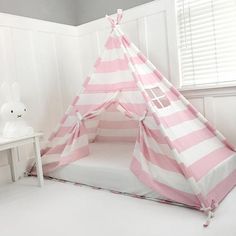 a pink and white striped teepee tent in a child's room with a small table