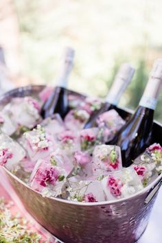 several bottles of wine are in an ice bucket with flowers on the inside and pink ribbon around it