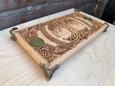 a decorative wooden cutting board with an intricate design on the front and back cover, sitting on a table next to a brick wall