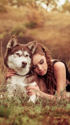 a beautiful young woman cuddles with her husky dog in the grass at sunset