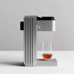 a coffee maker with a glass in front of it on a white countertop next to a gray wall