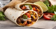 two burritos with meat, cheese and vegetables on paper next to a glass of water