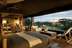 a bedroom with a large window and a bed in front of the glass wall that looks out onto an open field