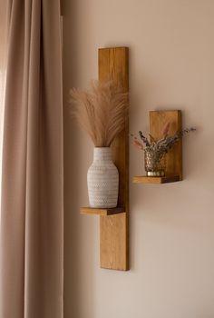 two wooden shelves with vases and plants on them in front of a curtained window